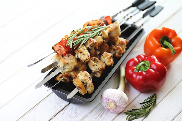 Kebab cuit sur des brochettes en métal avec des légumes servis sur une table blanche