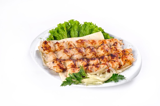 Kebab fait maison sur des brochettes avec du pain pita, des oignons, du chou, des légumes, sur une plaque blanche sur un fond blanc isolé.