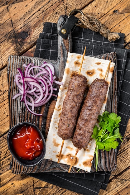 Kefta kofta kebab traditionnel du Moyen-Orient à partir de viande hachée de boeuf et d'agneau grillés sur des brochettes servies avec du pain plat et de l'oignon Fond en bois Vue de dessus