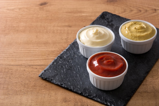 Ketchup, moutarde et mayonnaise dans des bols sur une table en bois