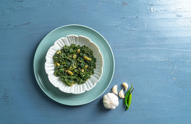 Keto diet food curry d'épinards dans un bol blanc et une assiette bleue avec de l'ail et des piments sur une table en bois bleu