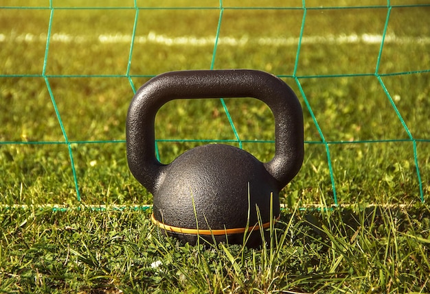 Kettlebell debout sur l'herbe avec filet et terrain de sport derrière