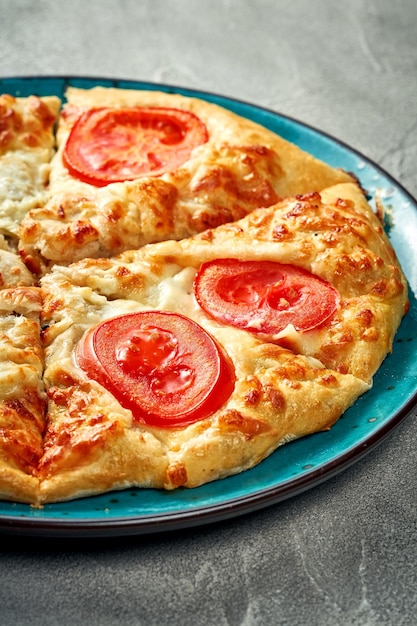 Khachapuri avec fromage fondu salé et tomate dans une assiette Fond de béton