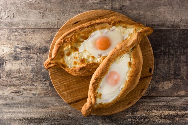 Khachapuri géorgien traditionnel Adjarien avec fromage et oeuf sur table en bois