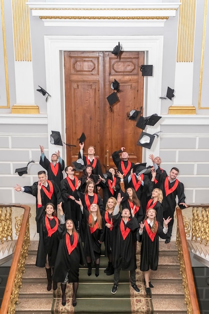 Photo kharkov, ukraine - 27 novembre 2018 : des étudiants diplômés en robes jettent des casquettes, debout à l'escalier de l'université