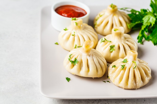 Khinkali de boulettes traditionnelles géorgiennes avec de la viande et des légumes verts sur un plat blanc.