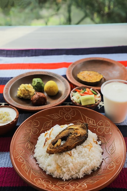 Khuder Bhat Hilsa Khichuri Combo avec salade d'aubergines borhani et Chui Pitha servi dans un plat isolé sur un tapis vue de dessus de la nourriture indienne et bangladaise