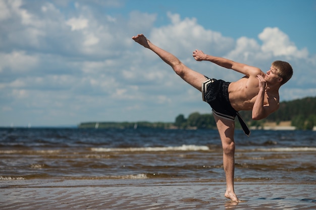 Kickboxer donne un coup de pied en plein air en été contre la mer.