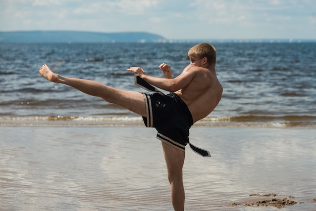 Kickboxer donne un coup de pied en plein air en été contre la mer.