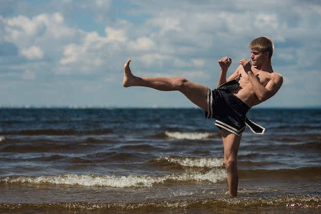 Kickboxer donne un coup de pied en plein air en été contre la mer.