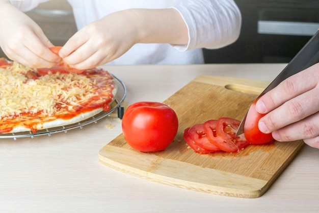 Kid aide son père à cuisiner des pizzas maison. Passe-temps en famille pendant la quarantaine. Processus de cuisson de pizza par enfant. Restez à la maison, la distance sociale et l'auto-isolement.