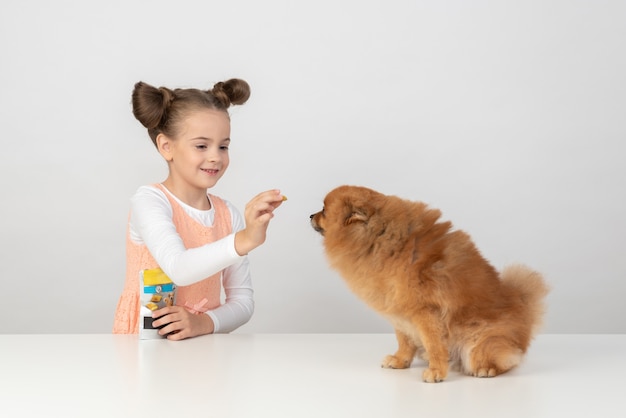 Photo kid fille donnant une friandise pour chien à un spitz