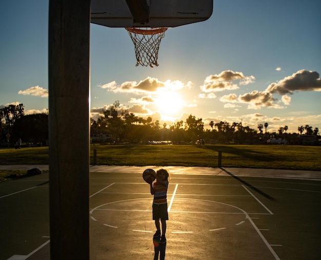 Kid garçon concentré sur jouer au basket-ball silhouette au coucher du soleil