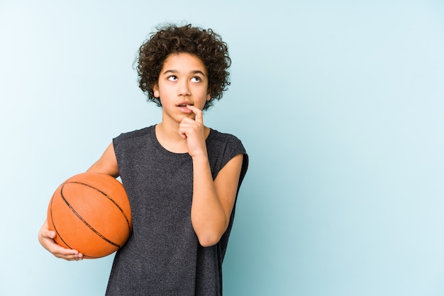 Kid garçon jouant au basket-ball sur le mur bleu détendu penser à quelque chose en regardant un espace vide.