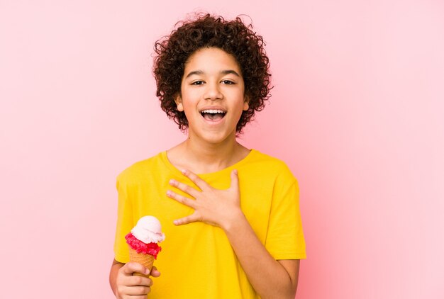 Kid garçon tenant une crème glacée isolée rit à haute voix en gardant la main sur la poitrine.