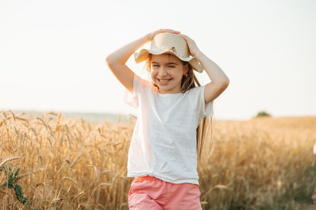 Kid girl with hat happy sourit magnifiquement tandis que dans l'enfance d'un champ de blé doré à la campagne ...