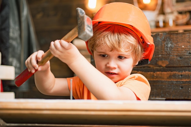 Kid in hard hat holding planche de bois et marteau. Enfant ingénieur avec marteau de charpentier sur bois.