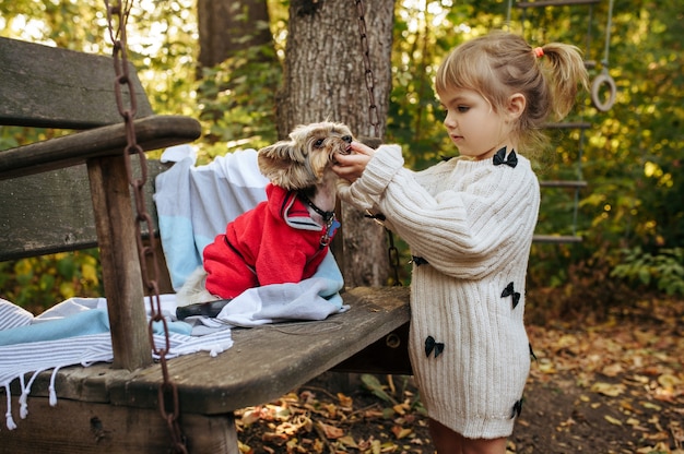 Kid jouer avec un chien drôle sur une grande chaise en bois dans le jardin. Enfant de sexe féminin avec chiot pose sur la cour. enfance heureuse