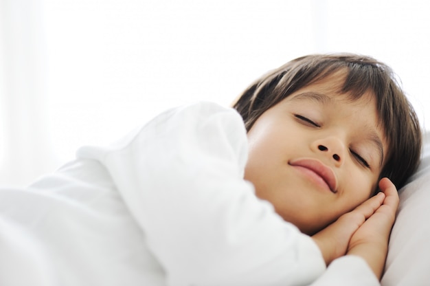 Kid sur le lit, l&#39;heure du coucher heureuse dans la chambre blanche