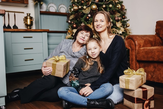 Kid avec maman et grand-mère sont assis serrés contre un arbre de Noël.