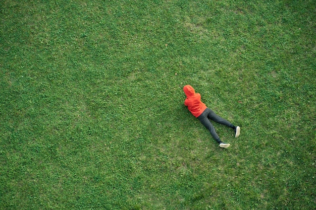 Kid porté en sweat à capuche rouge se trouve sur l'herbe, vue de dessus, espace copie