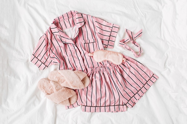 Kit de couchage pyjama avec chaussons en fourrure duveteuse. Robe de nuit rose classique à rayures au lit. Bonjour concept. Mise à plat, vue de dessus