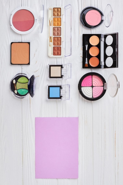 Kit de produits de maquillage, vue de dessus. Ensemble de fards à paupières multicolores à côté d'une feuille de papier vierge sur un fond en bois blanc. Cosmétiques de maquillage de mode.