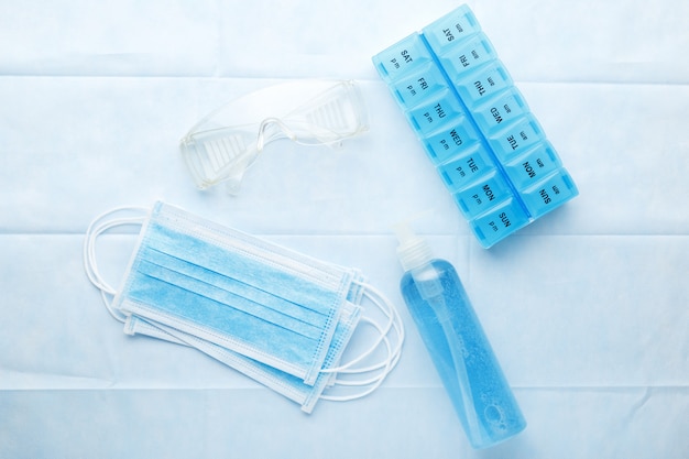 Kit de protection des travailleurs médicaux pour les médecins. Masque protecteur chirurgical, lunettes, gel antiseptique désinfectant pour les mains, boîte à pilules sur fond bleu.