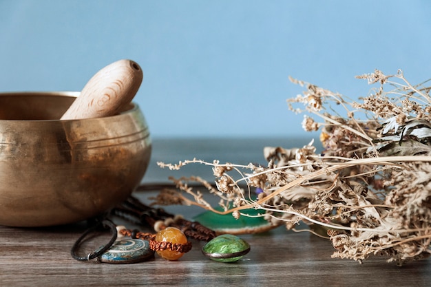 Kit de sorcière. Sur une table en bois se trouve un bol de métal jaune, de cristaux verts et orange et d'herbes sèches.