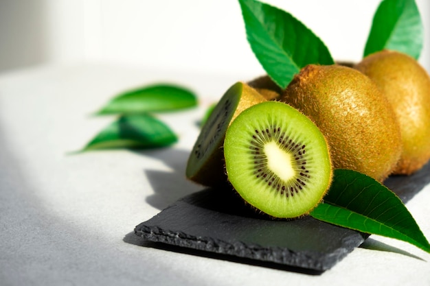 Photo kiwis mûrs au soleil tas de kiwis entiers avec des feuilles vertes et kiwi fraîchement coupé sur ardoise fruits biologiques sains pleins de vitamines et d'antioxydants