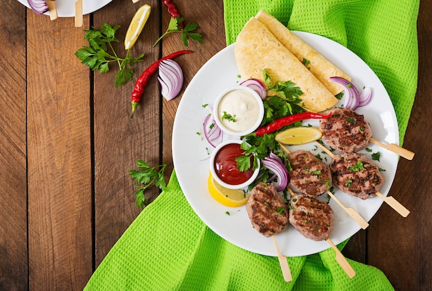 Kofta kebab appétissant (boulettes de viande) avec des tacos de sauce et de tortillas sur une assiette blanche