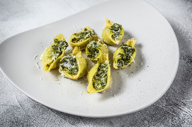 Konkiloni Pâtes coquilles géantes Conchiglioni farcis aux épinards sur une assiette. Fond blanc. Vue de dessus.