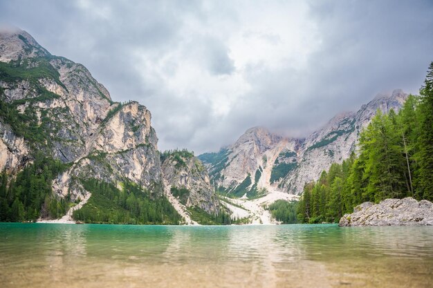 Photo le lac de braies entouré de forêts de pins et des chaînes rocheuses des dolomites par une journée nuageuse en italie