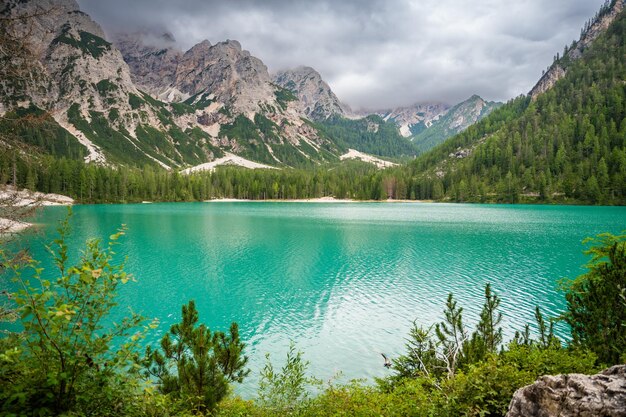 Le lac de Braies entouré de forêts de pins et des chaînes rocheuses des Dolomites par une journée nuageuse en Italie