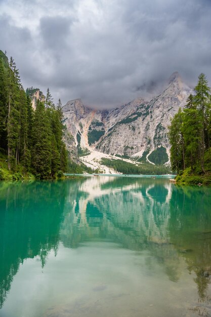 Photo le lac de braies entouré de forêts de pins et des chaînes rocheuses des dolomites par une journée nuageuse en italie