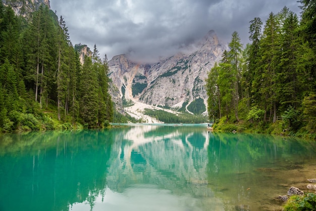 Photo le lac de braies entouré de forêts de pins et des chaînes rocheuses des dolomites par une journée nuageuse en italie