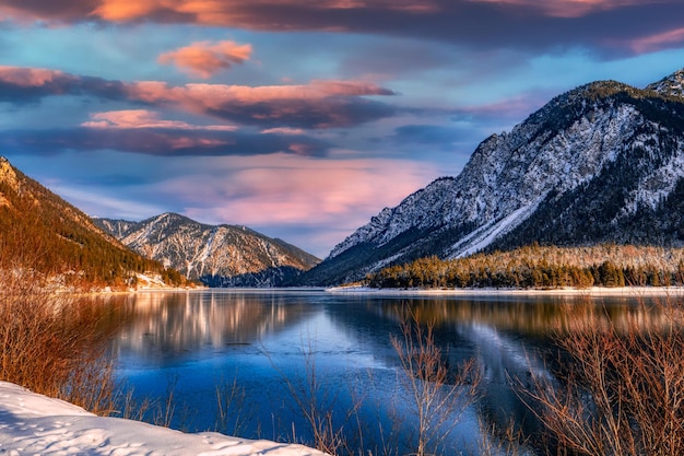 Lac gelé sur fond de forêt de montagne au coucher du soleil