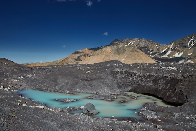 Le lac glaciaire turquoise est niché parmi les morènes sombres sous une chaîne de montagnes et un ciel bleu.