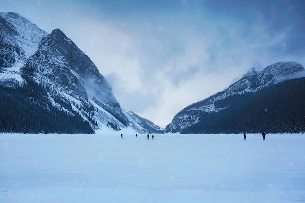 Lac Louise gelé avec des montagnes rocheuses et des touristes jouant au patin à glace dans une journée sombre le matin