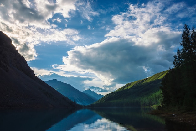 Lac de montagne fantomatique dans les hautes terres au début de la matinée. Belles silhouettes brumeuses de montagnes et de nuages se reflètent dans la surface de l'eau claire. Fumée de feux de camp. Magnifique paysage de nature majestueuse.