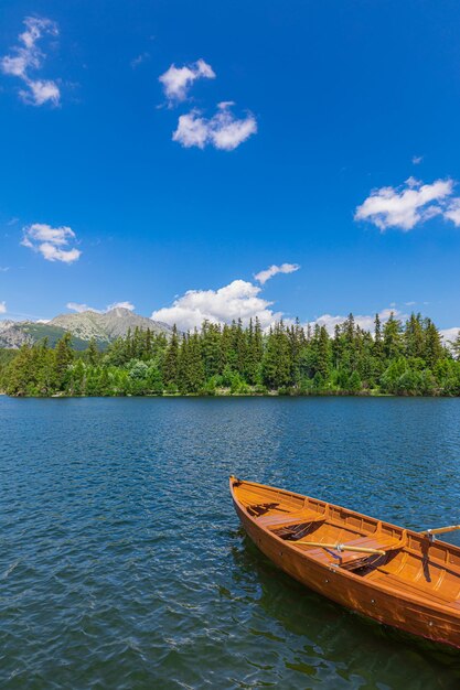 Photo lac de montagne avec forêt de conifères bateau en bois ciel bleu ensoleillé arrière-plan de voyage de liberté idyllique