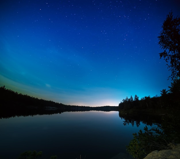 Lac de nuit avec un ciel étoilé incroyable et des reflets dans l'eau. Les extérieurs naturels voyagent sur fond sombre.