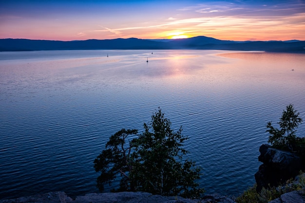 Lac pittoresque et rivage rocheux après le coucher du soleil