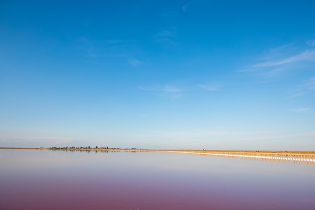 Lac rose et plage de sable avec une baie sous un ciel bleu avec des nuages