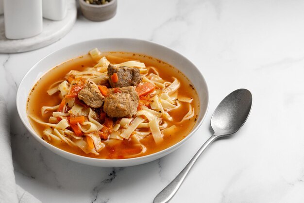 Lagman. La soupe nationale ouzbek avec des nouilles et des morceaux de viande, des légumes frits. Bouchent la soupe. Plaque blanche et fond blanc