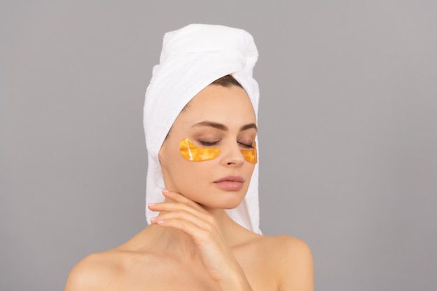 Laisser la peau respirer cosmétologie de la peau hydratante jeune femme en serviette éponge utiliser patch beauté dans le spa appliquer un masque antifatigue doré fille réduire les poches sous les yeux soins de la peau cosmétique au collagène du visage