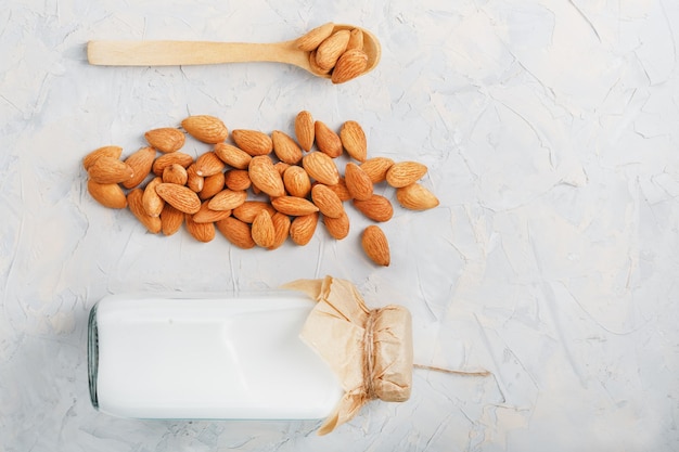 Lait d'amande dans une bouteille avec une poignée de graines et une cuillère en bois sur fond clair. Vue de dessus