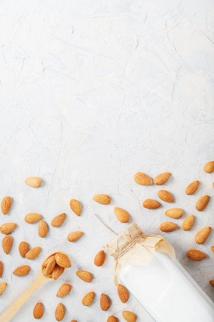 Lait d'amande dans une bouteille en verre sur fond clair avec une dispersion de noyaux de graines et une cuillère en bois.