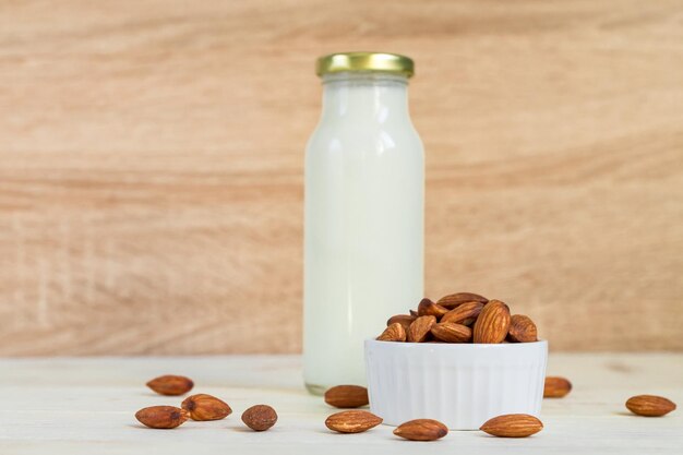 Le lait d'amande fait maison dans une bouteille et des noix dans un bol de porcelaine blanche sur fond de bois