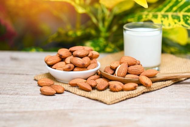 Lait d'amande et noix d'amandes sur bol blanc avec feuille verte sur fond de sac Délicieuses amandes douces sur la table en bois Noix d'amandes grillées pour une alimentation saine